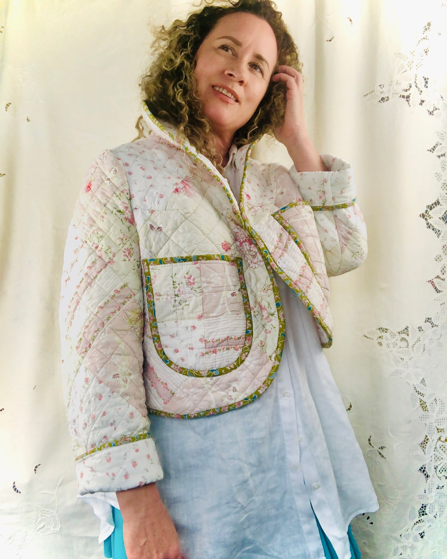Woman wearing a quilted jacket with floral patterns and patch pockets against a white curtain background