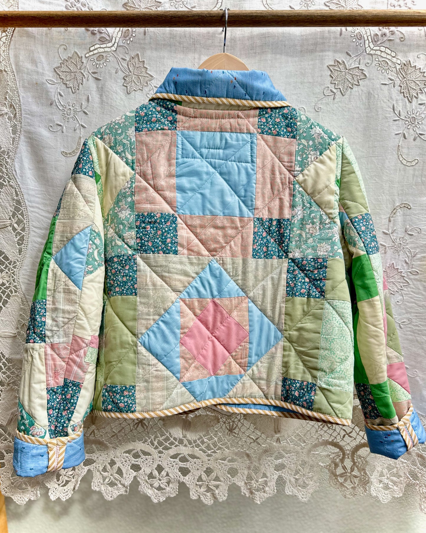 Back view of a quilted jacket with patchwork design on a lace curtain background
