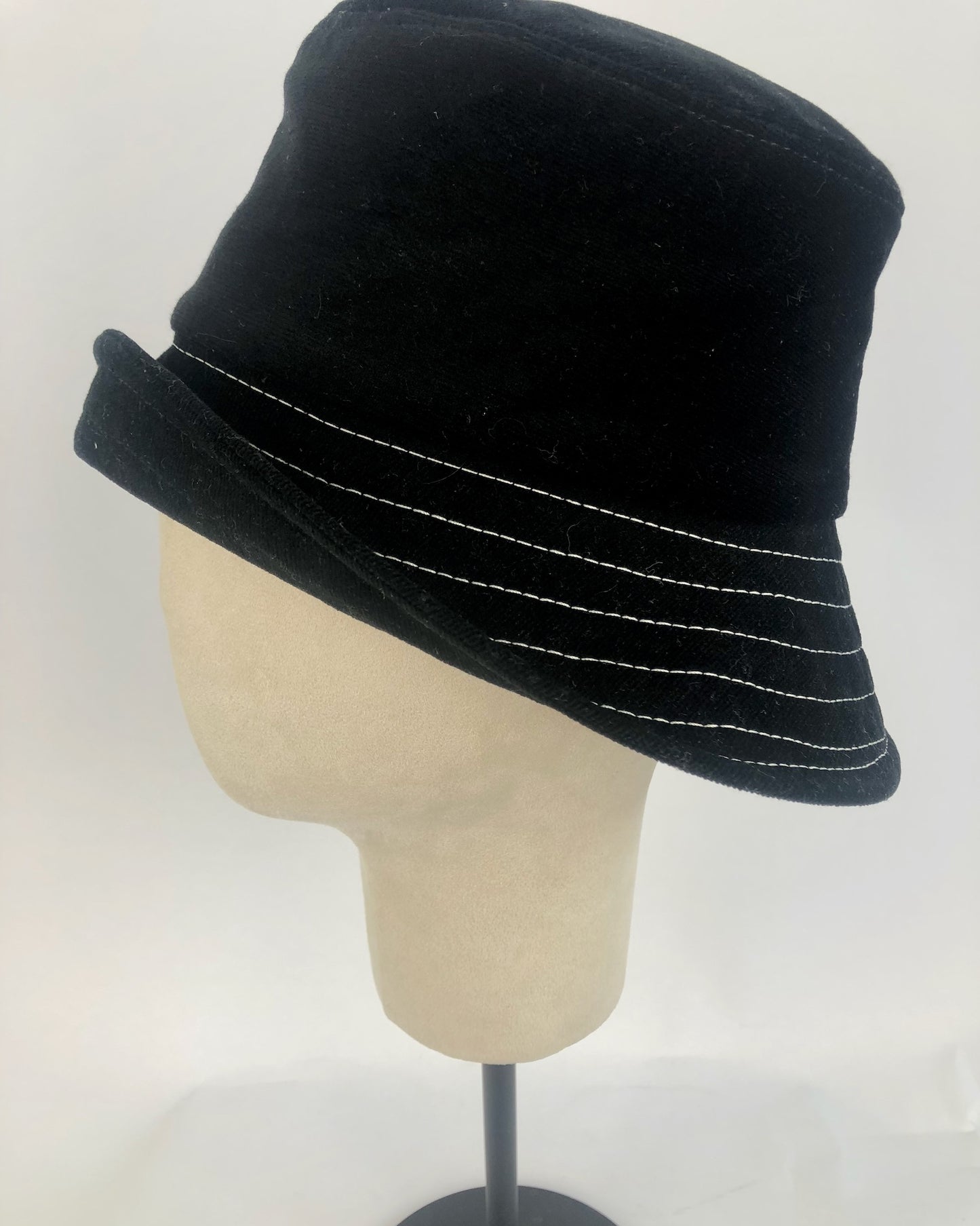 Minimalist black bucket hat made of corduroy, featuring parallel white stitching along the brim for a sleek, modern look.