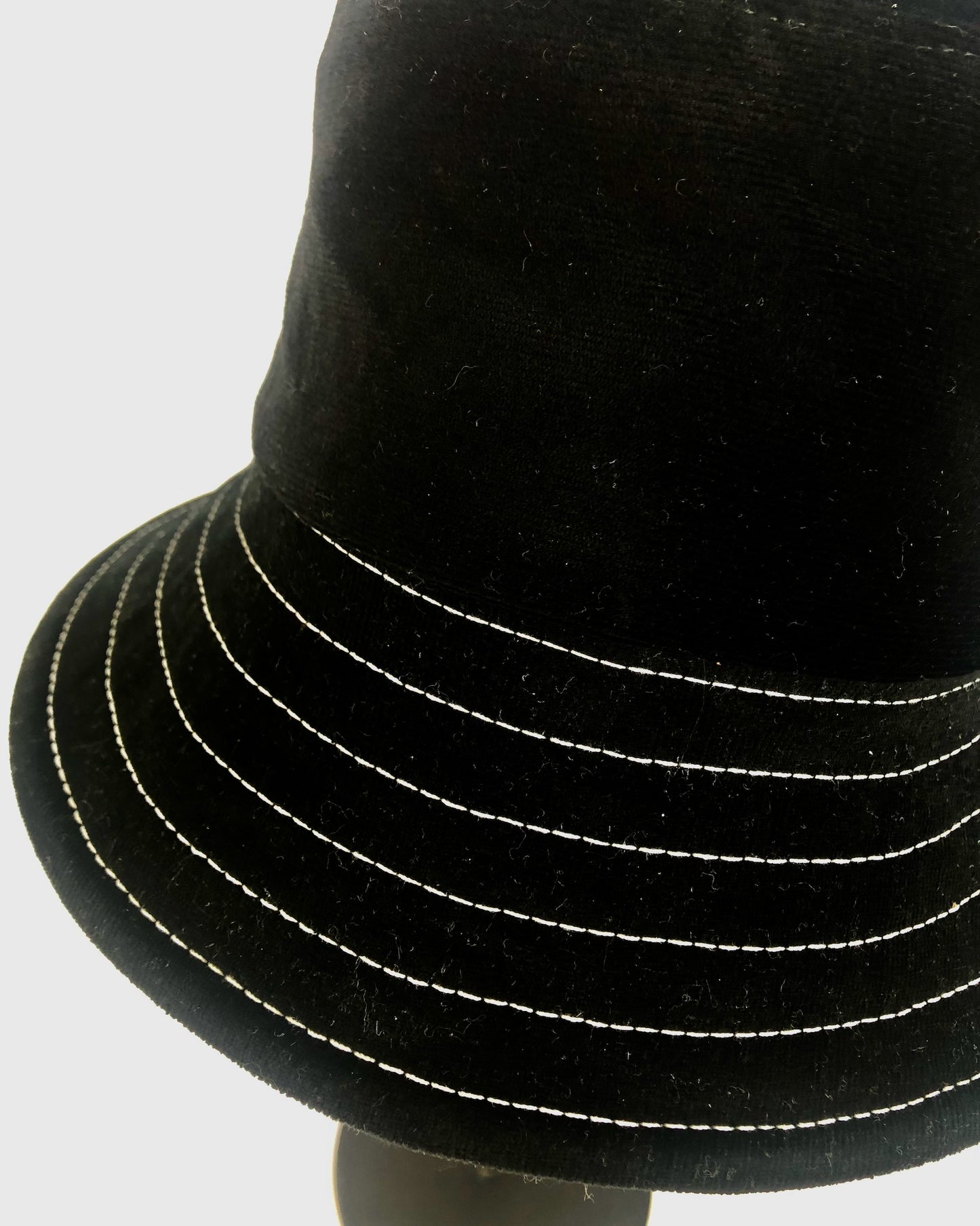 Textured black corduroy bucket hat with fine white stitch detailing, highlighting its classic yet contemporary style.