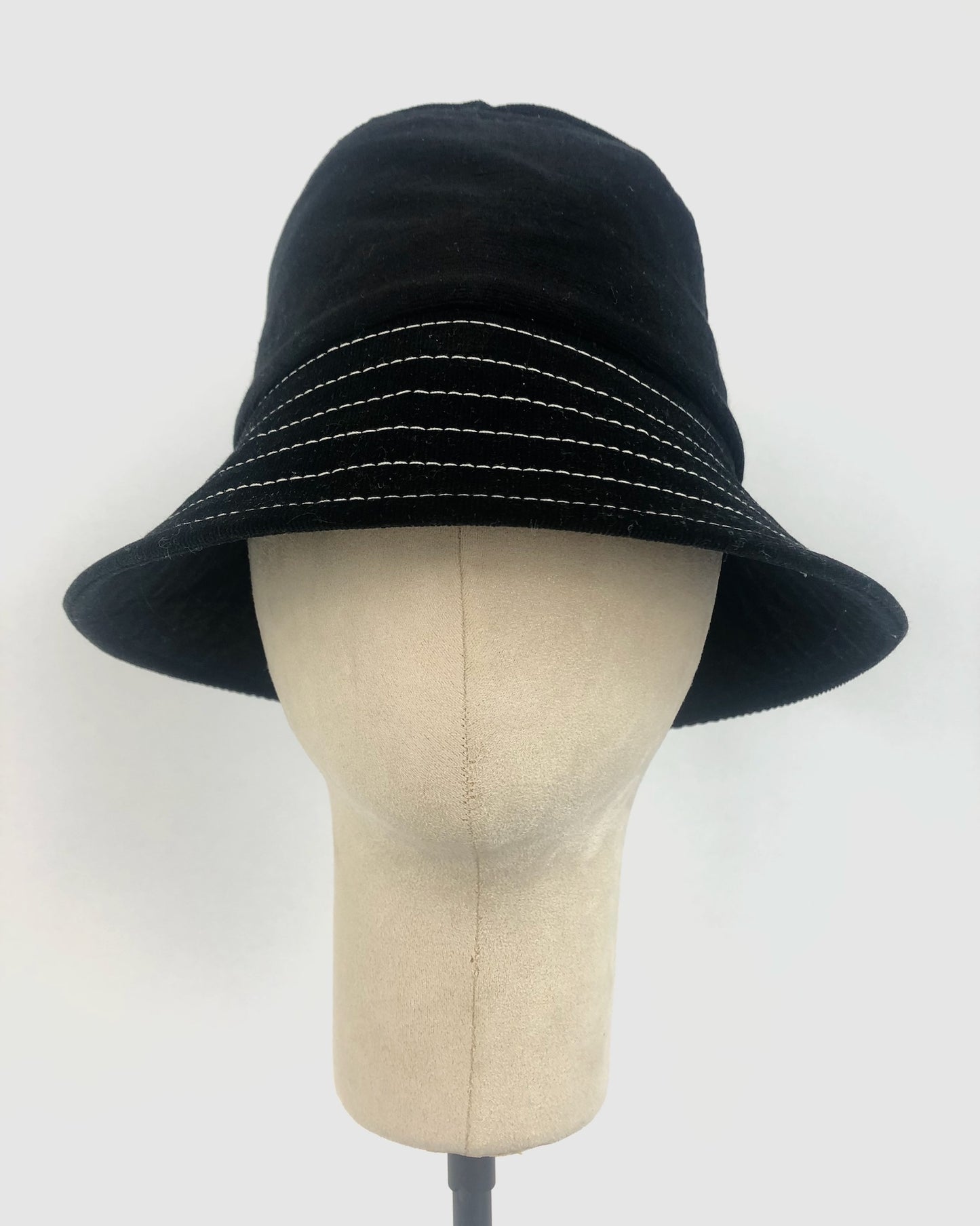 Close-up of a black corduroy bucket hat with evenly spaced white contrast stitching around the brim, showcasing the fabric’s soft texture and structured design