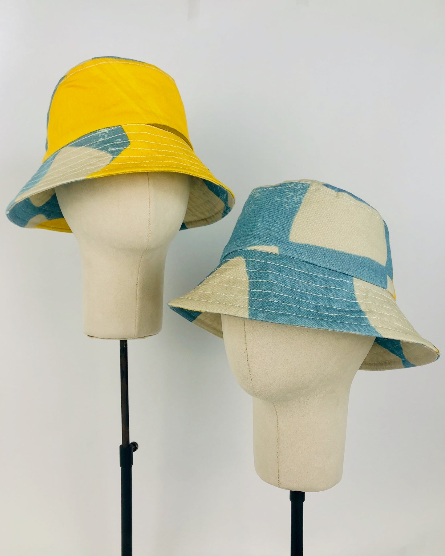 Two sky blue and yellow handmade hats on hat stands
