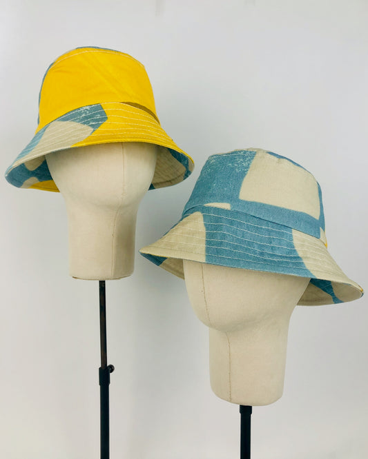 Two sky blue and yellow handmade hats on hat stands
