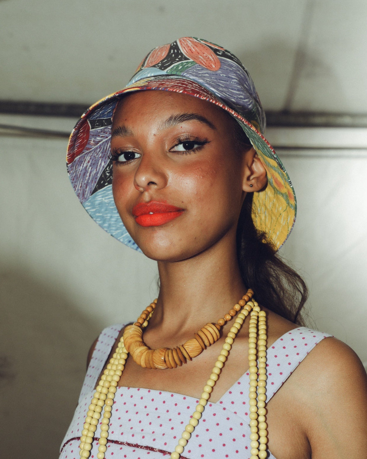 Model back stage wearing sustainable fashion with colourful bucket hat and a beaded necklace