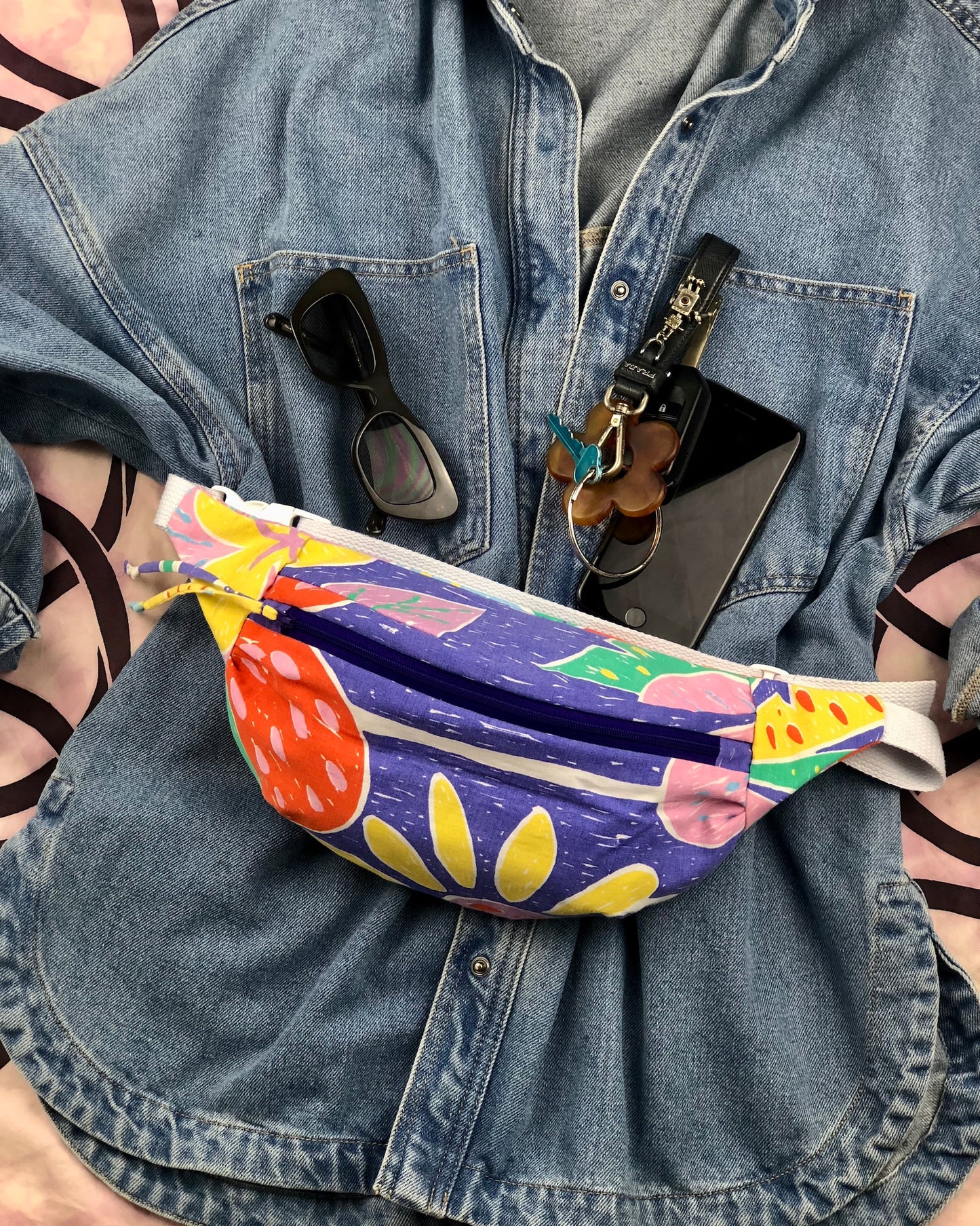 Flat lay of blue denim jacket with handmade bumbag made of ken done imitation print sheet and phone, keys and sunnies