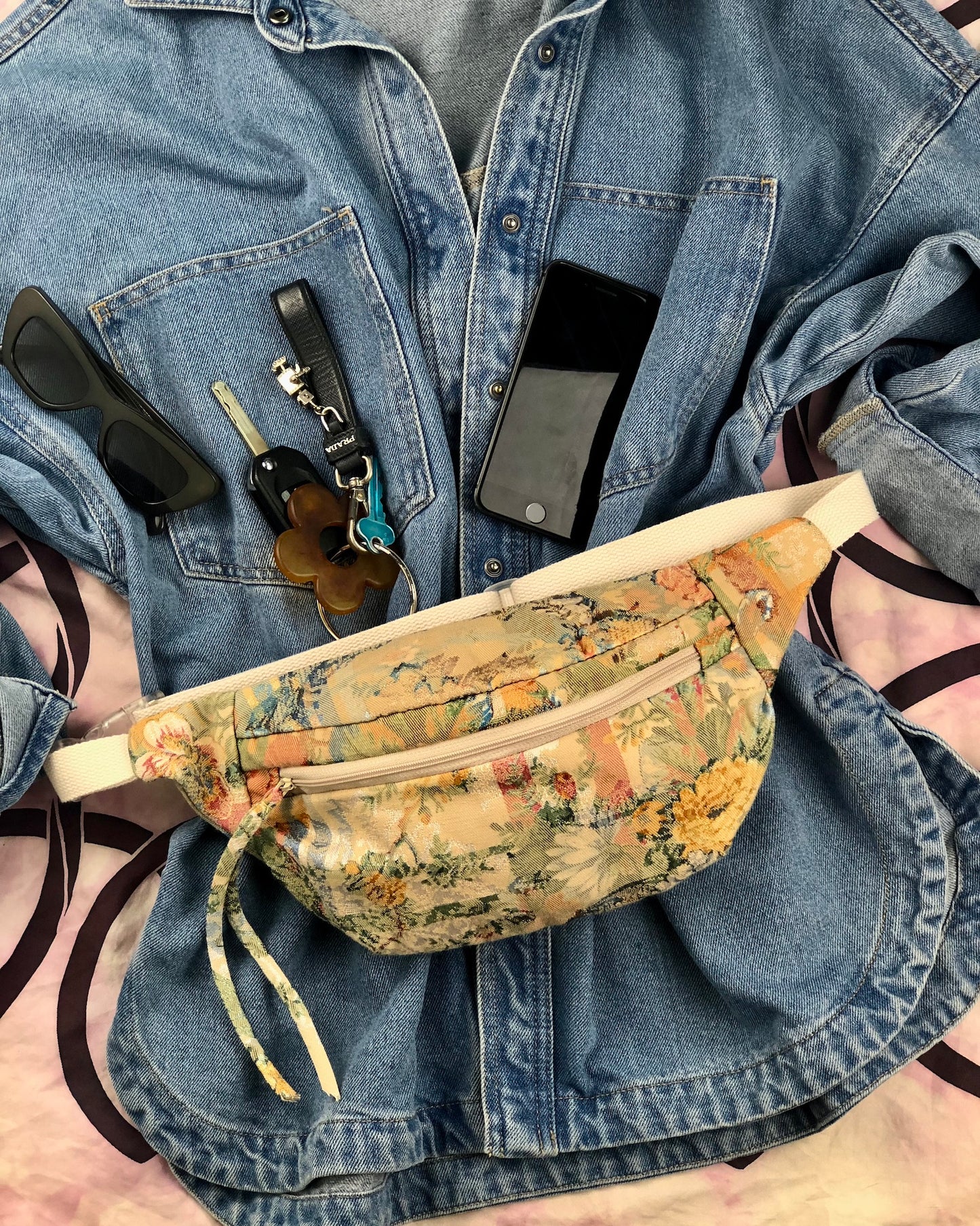 flat lay showing blue denim shirt with handmade bumbag made from vintage tapestry and sunglasses, phone and keys
