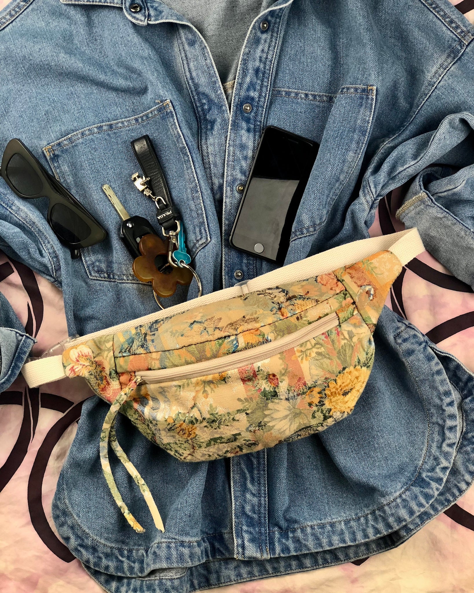 flat lay showing blue denim shirt with handmade bumbag made from vintage tapestry and sunglasses, phone and keys