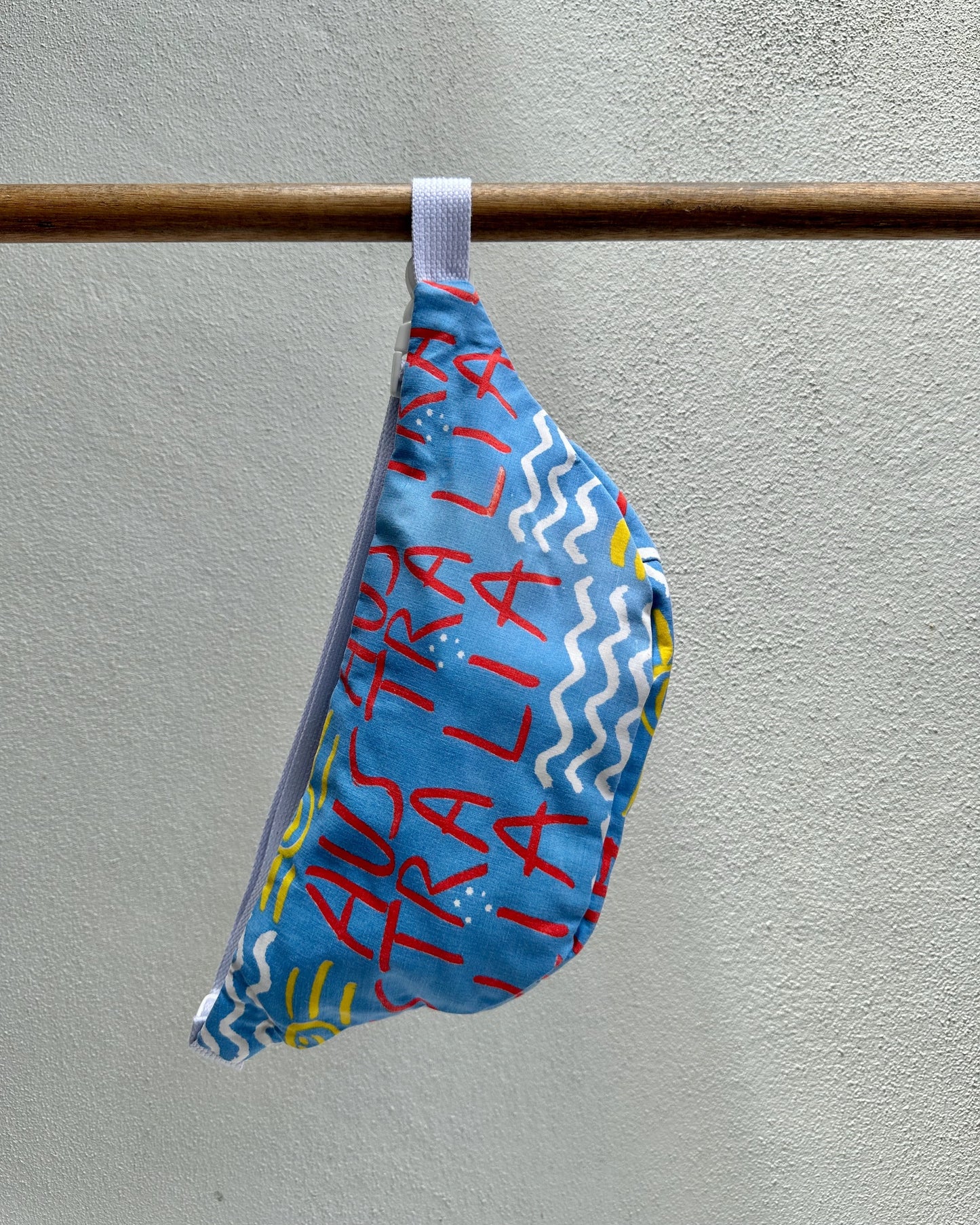 Blue bag with 'Australia' text hanging on a rod against a gray wall