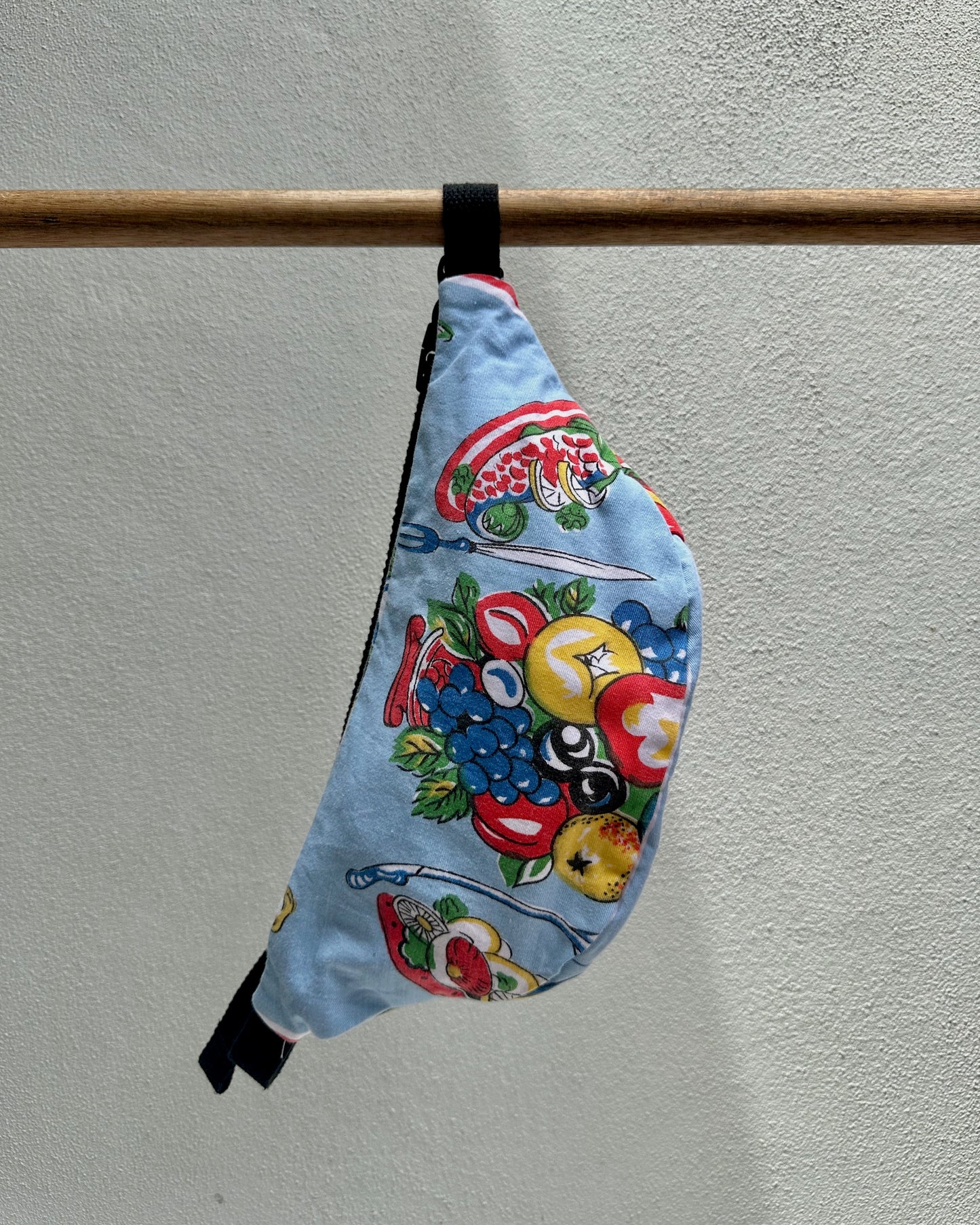 Colorful apron with cartoon designs hanging on a wooden rod against a light gray wall.