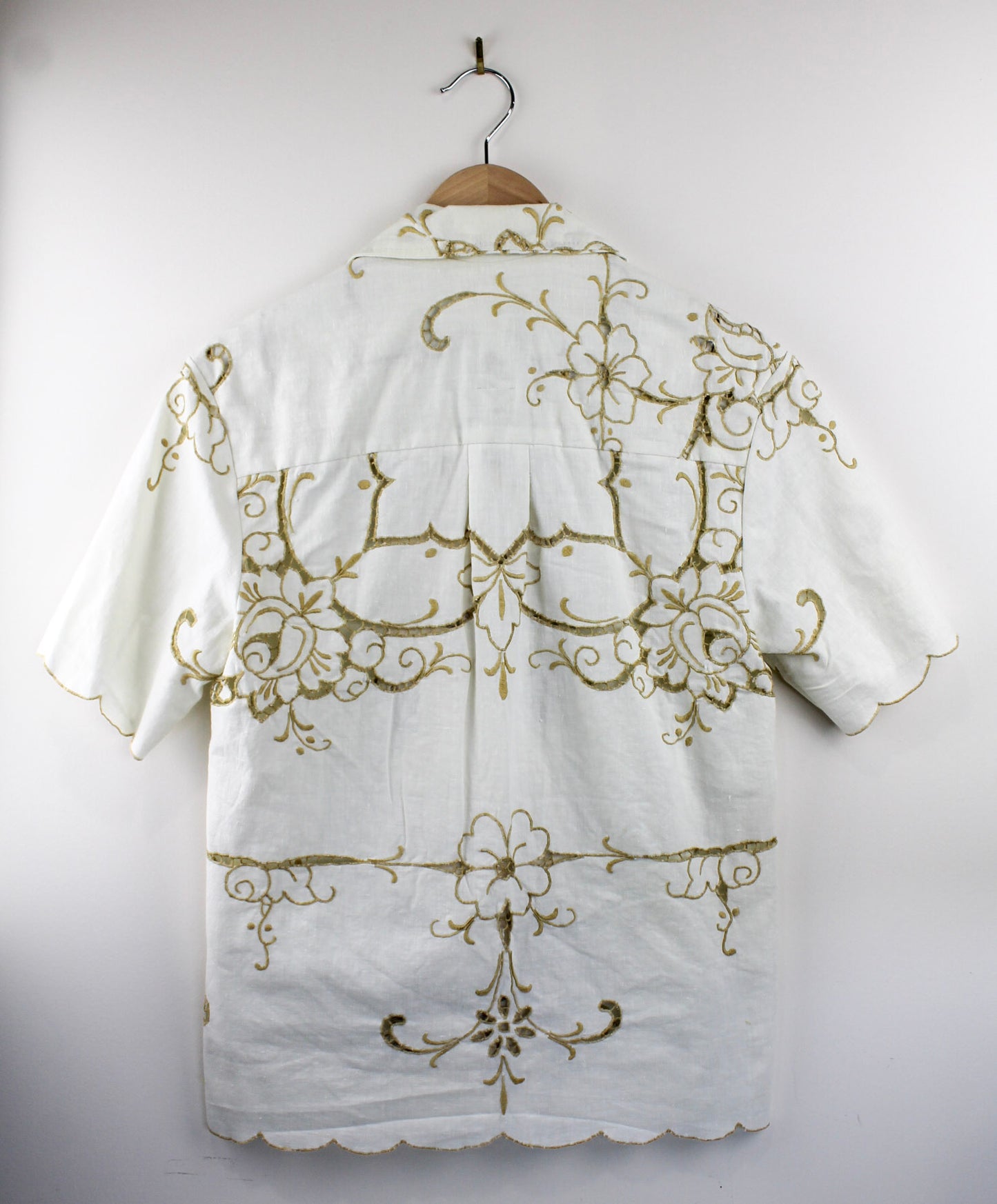 Back view of white collared shirt with gold embroidery on a hanger against a white background