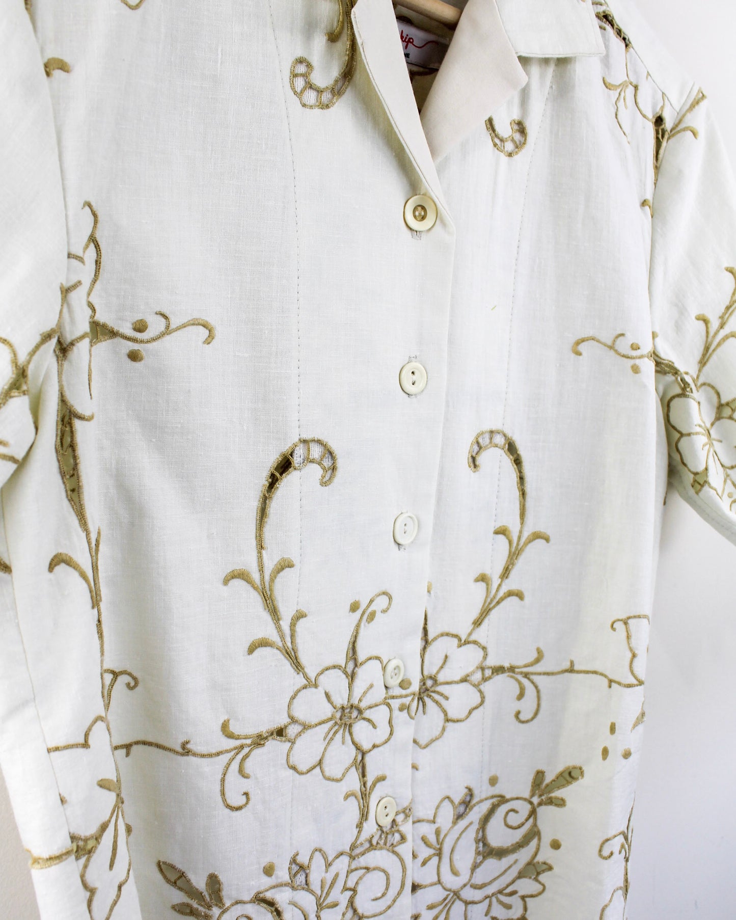 Close up detail of white shirt with gold floral embroidery and mismatched vintage buttons on a white background