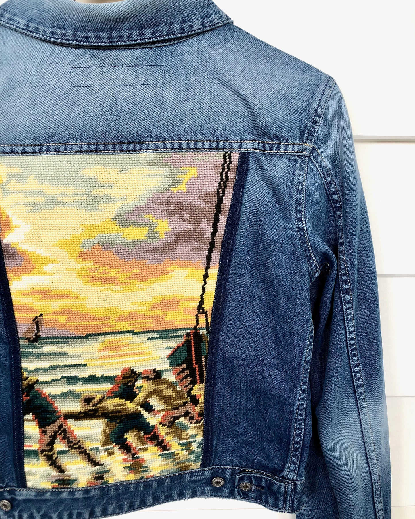 Close up detail showing needle point embroidery decorating an up cycled vintage denim jacket