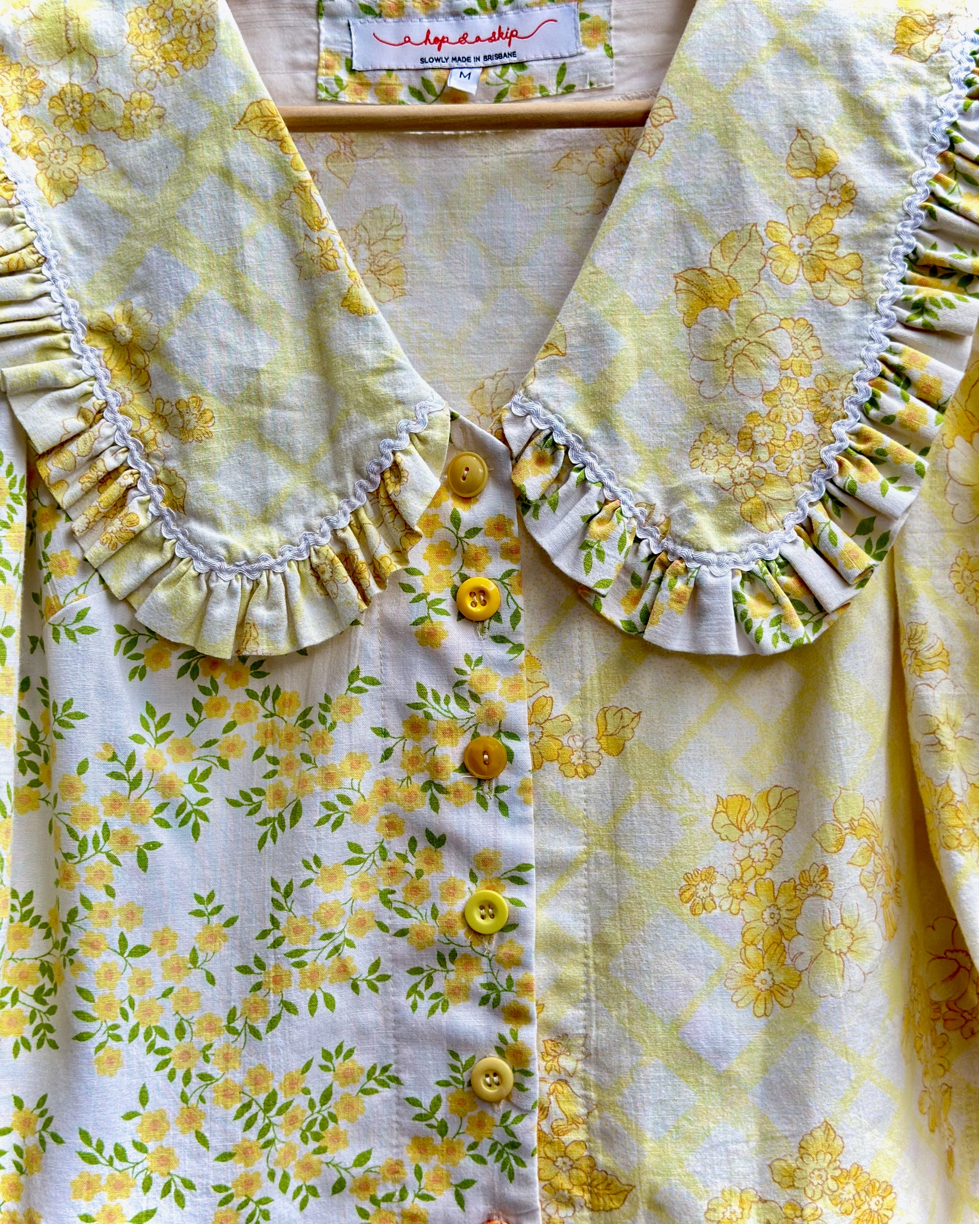 A close-up of a yellow and white floral blouse with a ruffled Peter Pan collar and button-front closure.
