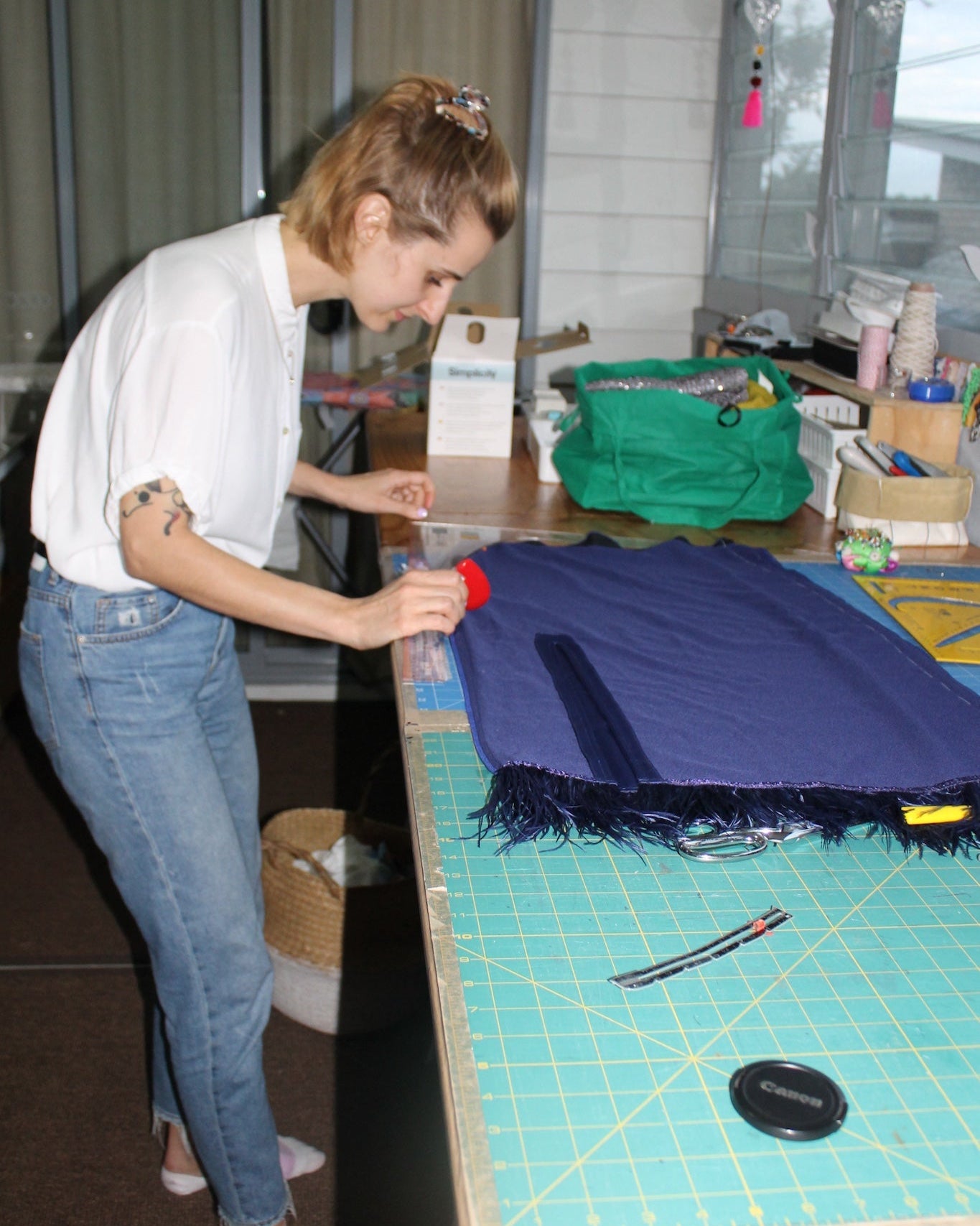 Person working on a blue fabric item at a table with various sewing tools and materials.