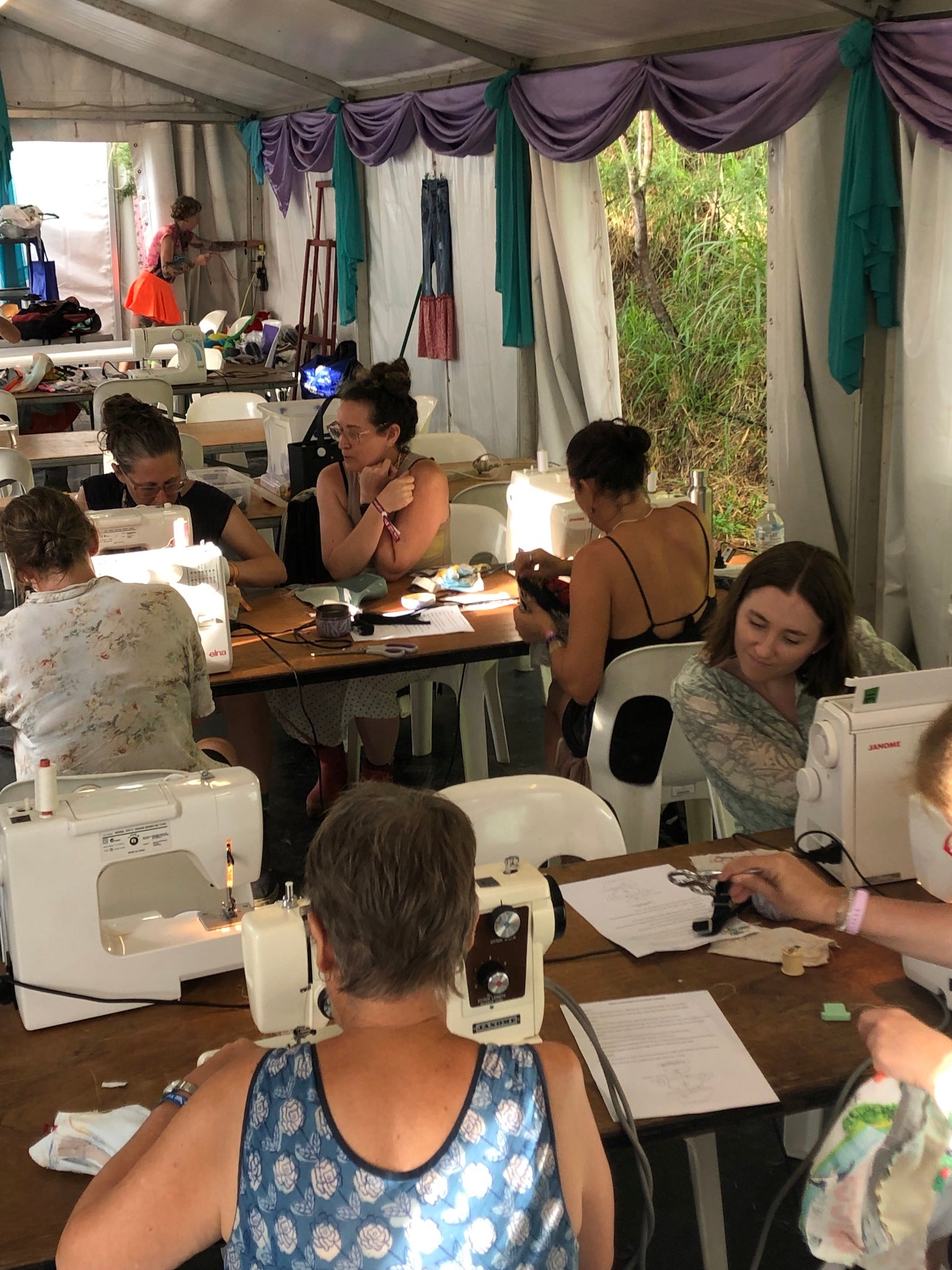 Group of people working on sewing machines in a tented workshop.