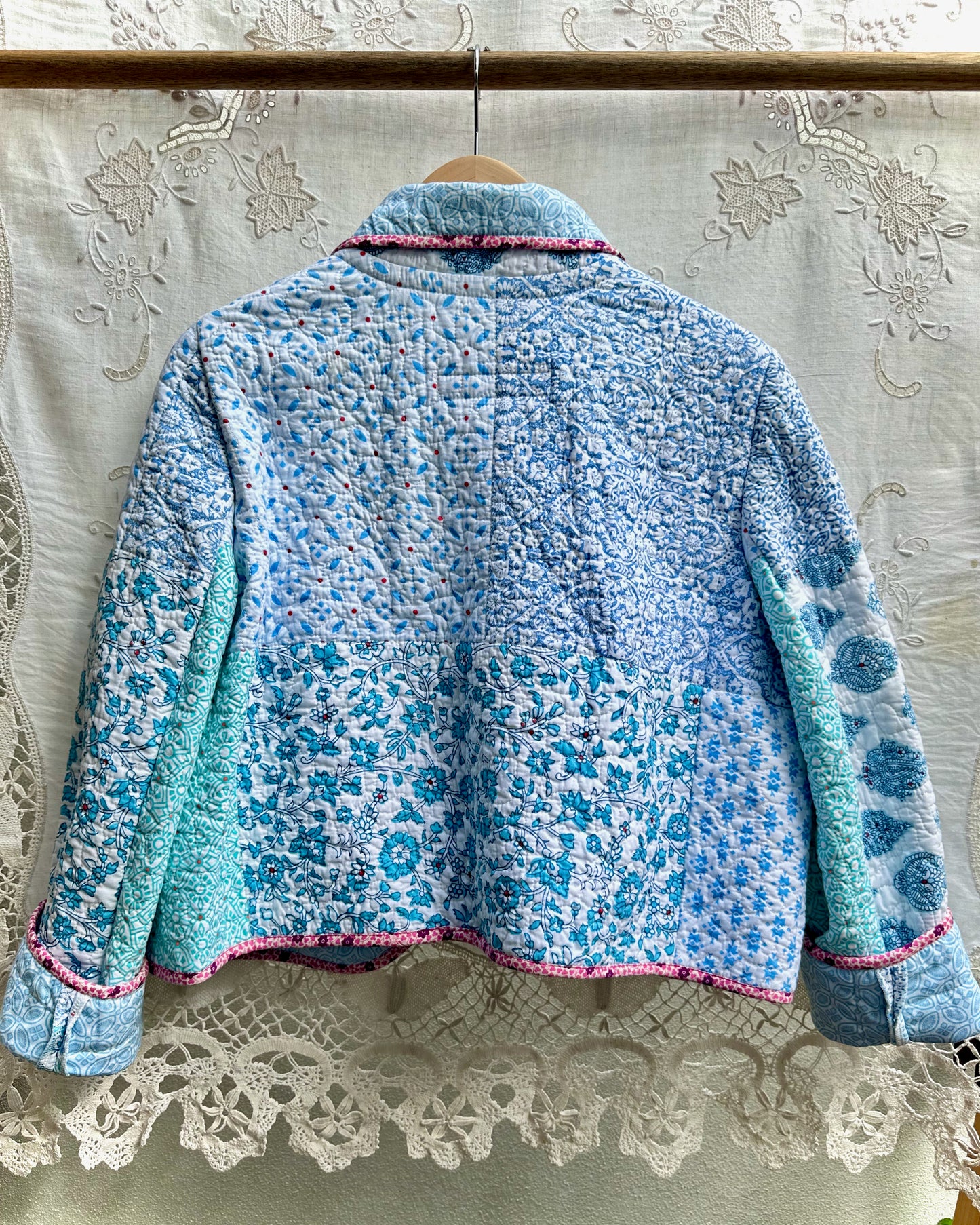 Blue floral-patterned jacket on a hanger against a lace curtain background