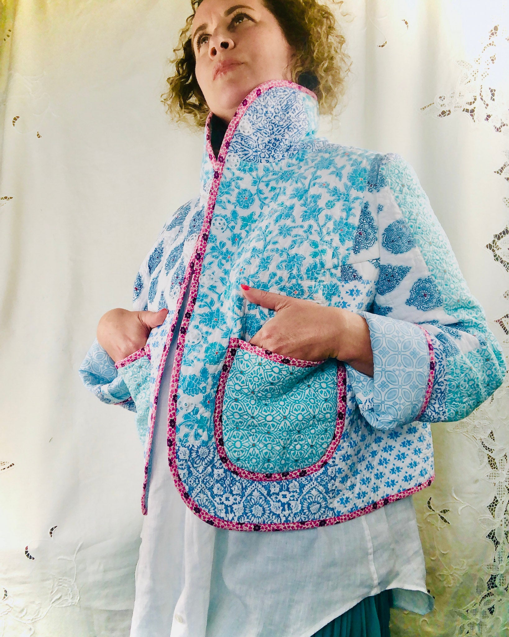 Woman wearing a blue floral patterned jacket against a white curtain background