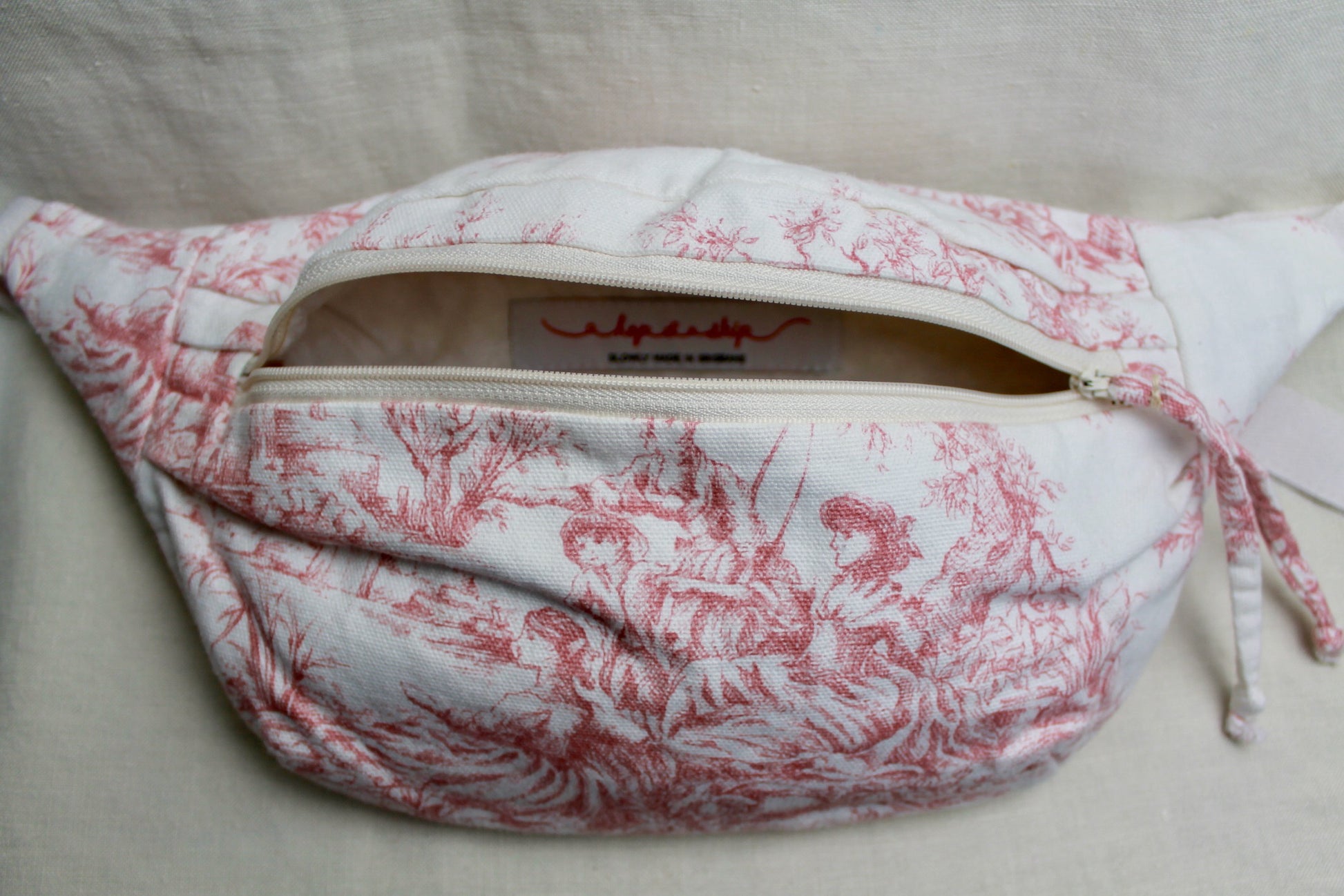 Front view of handmade toile du jouy bumbag featuring pink pastoral illustrations on a white background