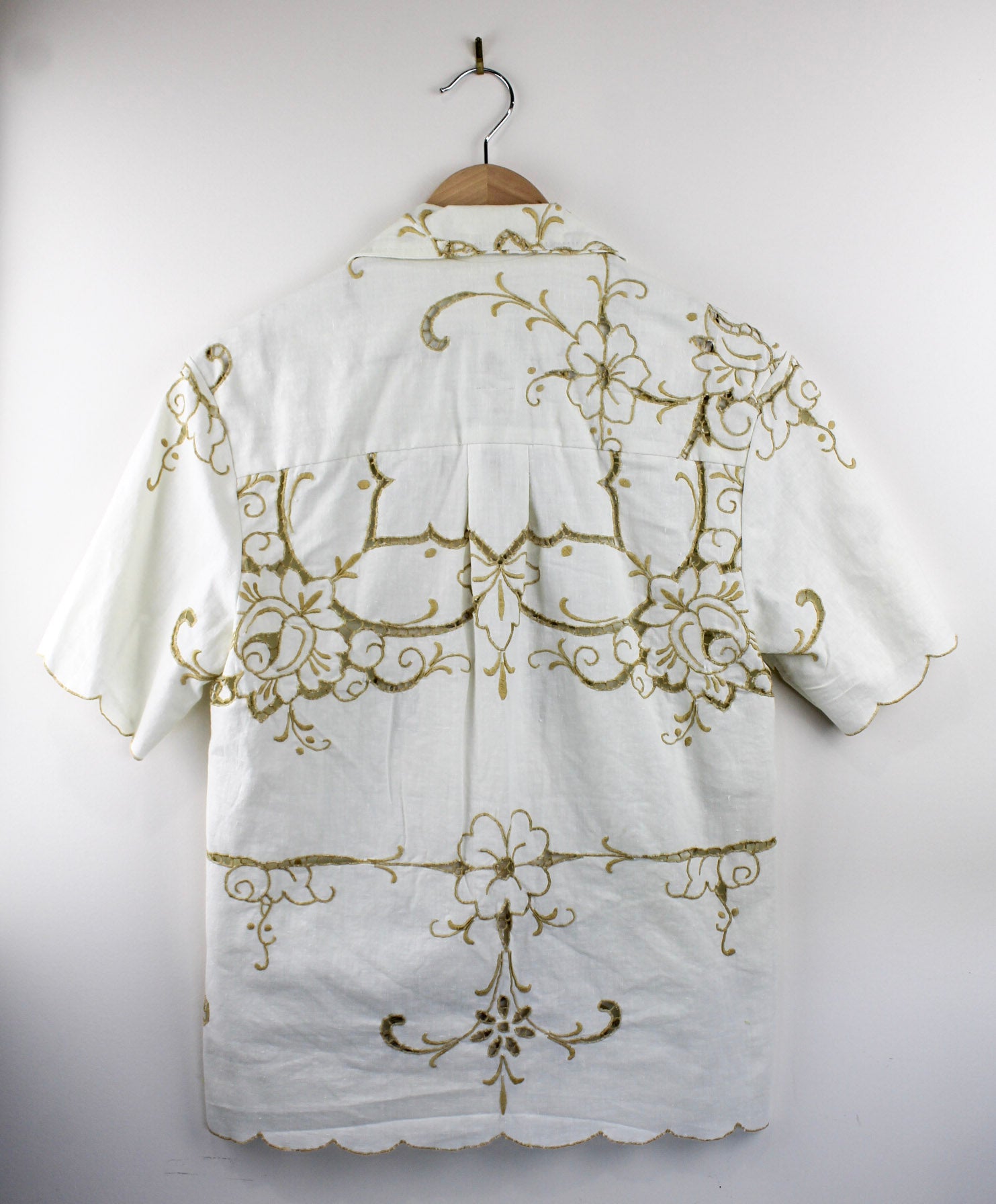 Back view of white collared shirt with gold embroidery on a hanger against a white background