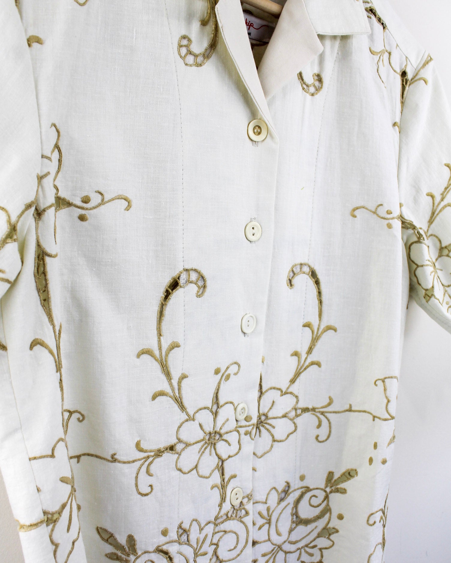 Close up detail of white shirt with gold floral embroidery and mismatched vintage buttons on a white background