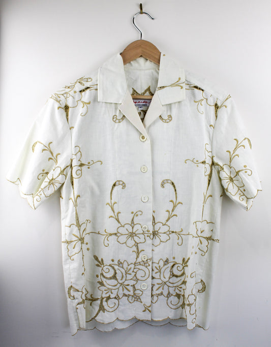White shirt made from vintage linen with gold embroidery on a wooden hanger against a white background