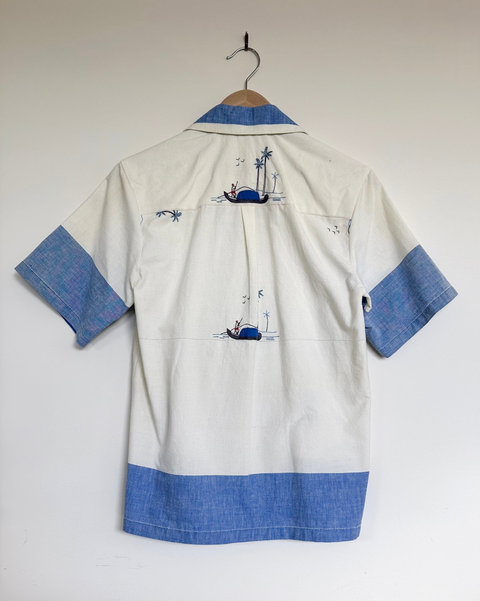 White shirt with blue accents and embroidered designs on a hanger against a white background