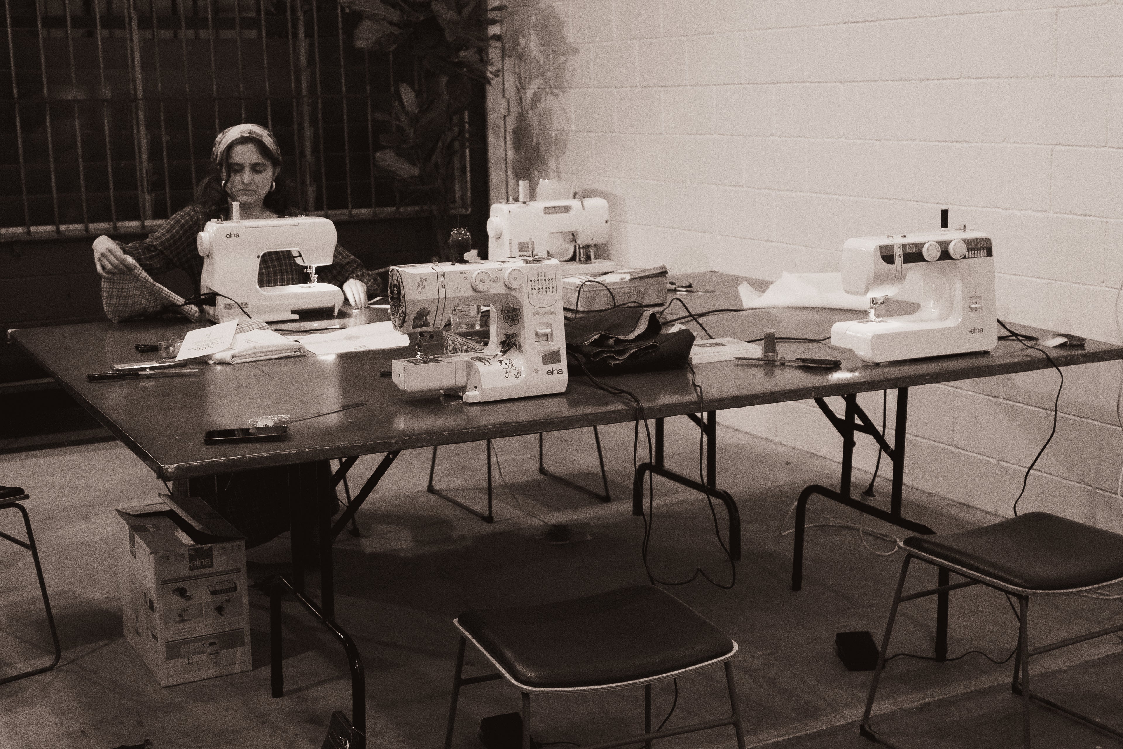 Person sitting at a table with multiple sewing machines in a room working on a sewing project