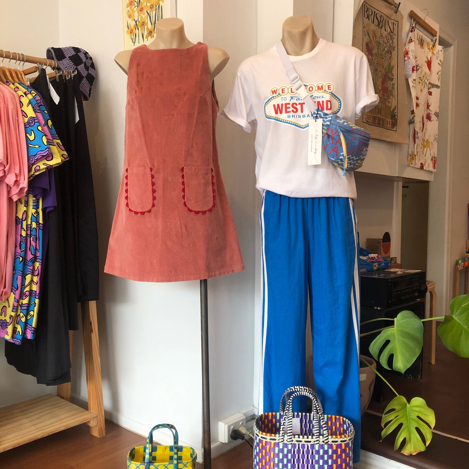 Mannequin wearing a white shirt with West End logo, blue pants, and a dusty pink corduroy retro dress styled with pali baskets.