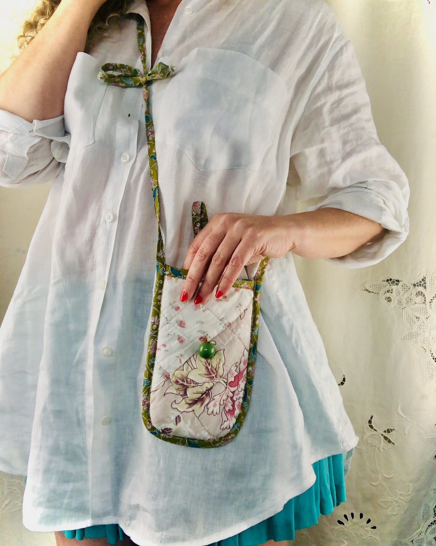 Person wearing a white shirt with a floral quilted phone bag