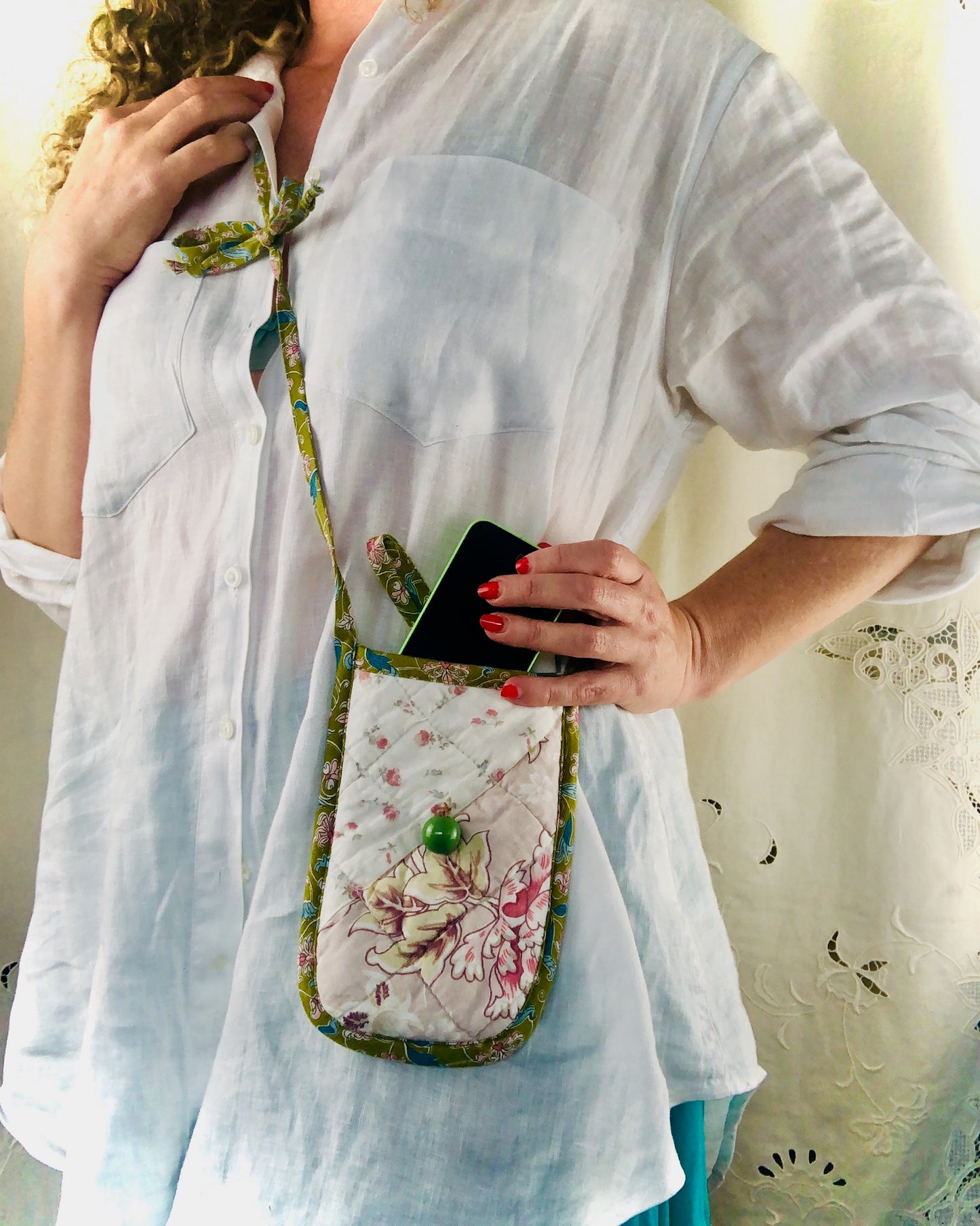 Person holding a floral-patterned pouch with a phone inside, wearing a light blue outfit.