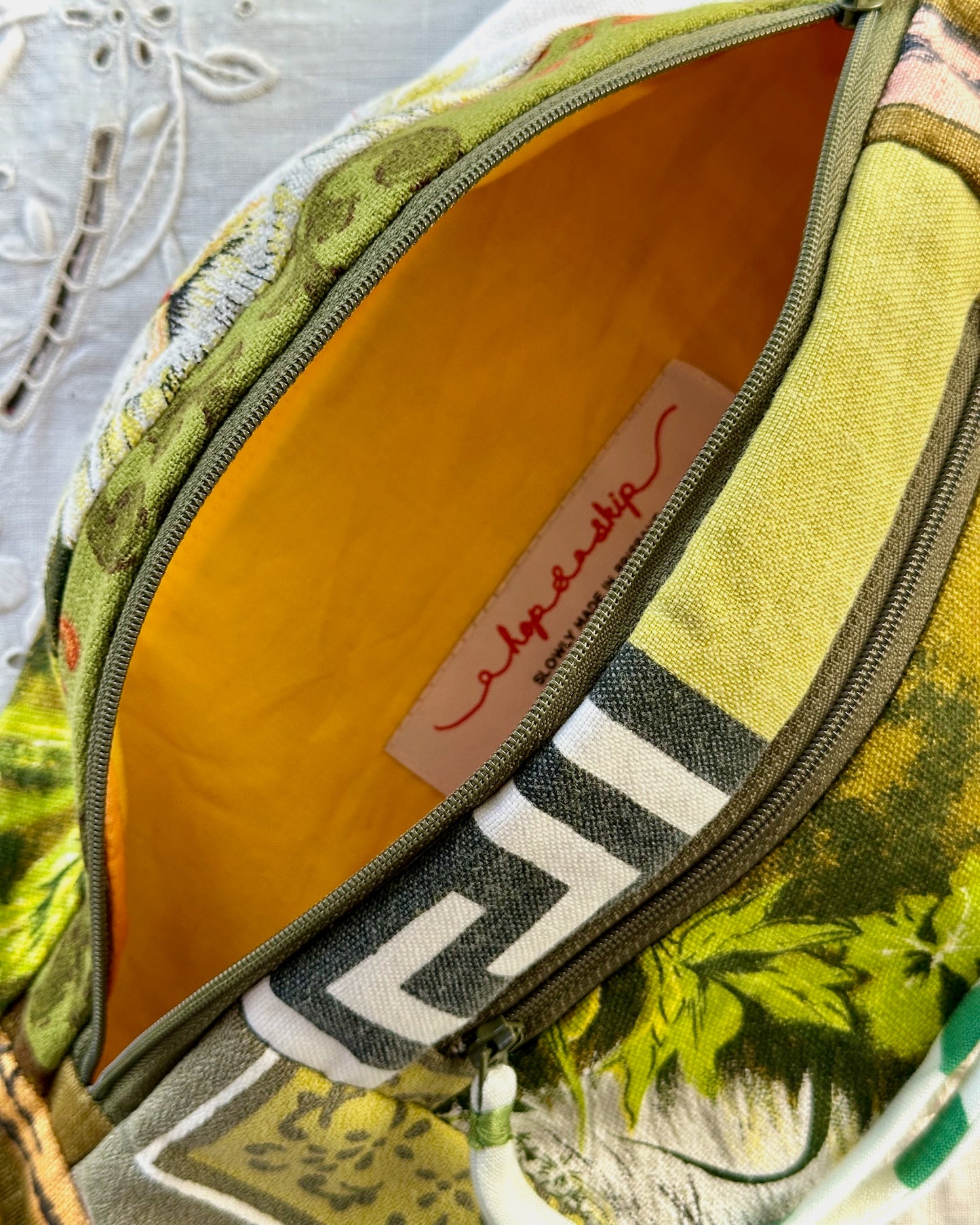 Close-up of a patterned fabric bag with a green and yellow botanical print, featuring a bright yellow interior lining and a white brand tag with red script.