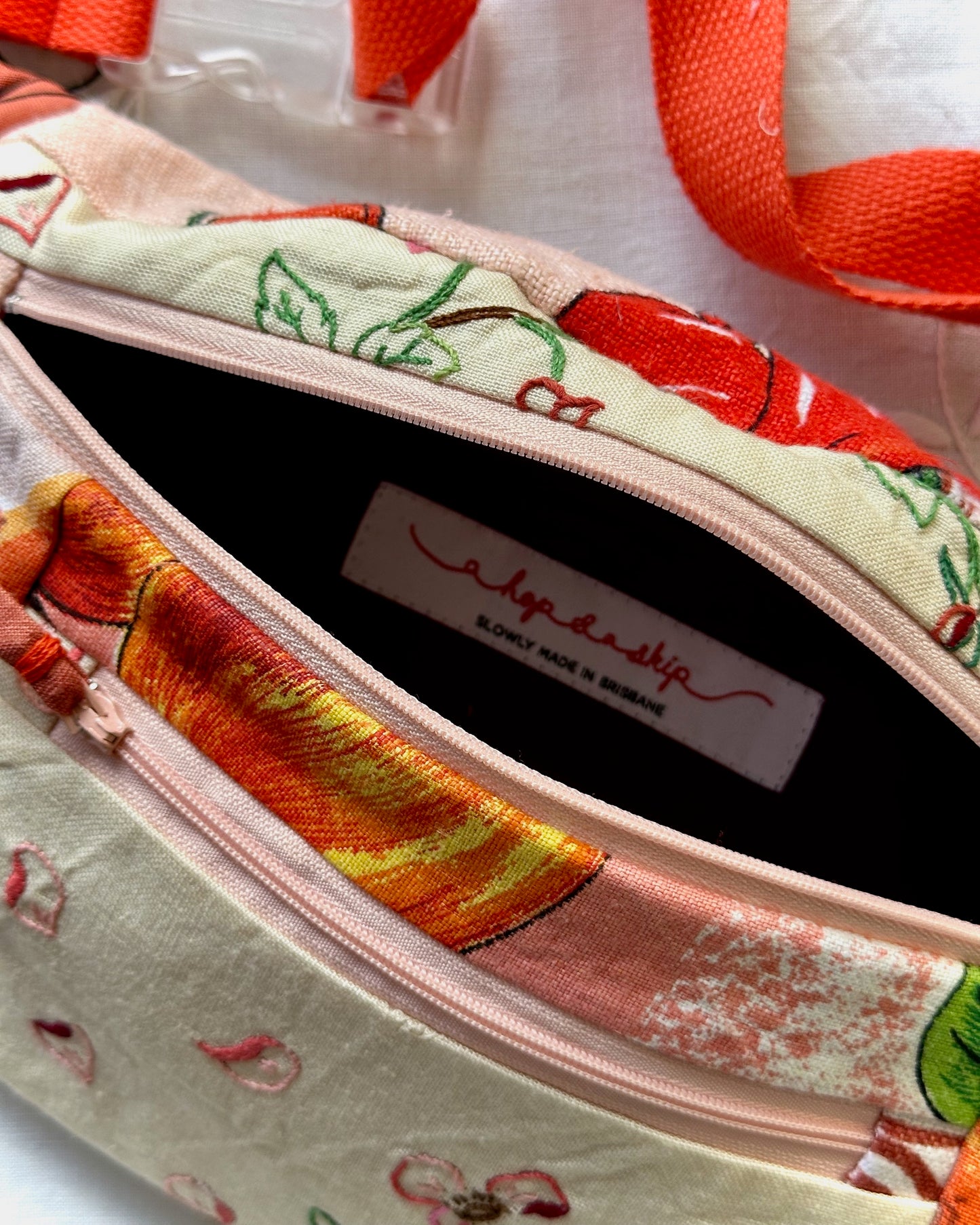 Close-up of a fabric zippered pouch with a colorful cherry and floral print, showing the interior lining and a visible 'a hop and a skip' brand label.