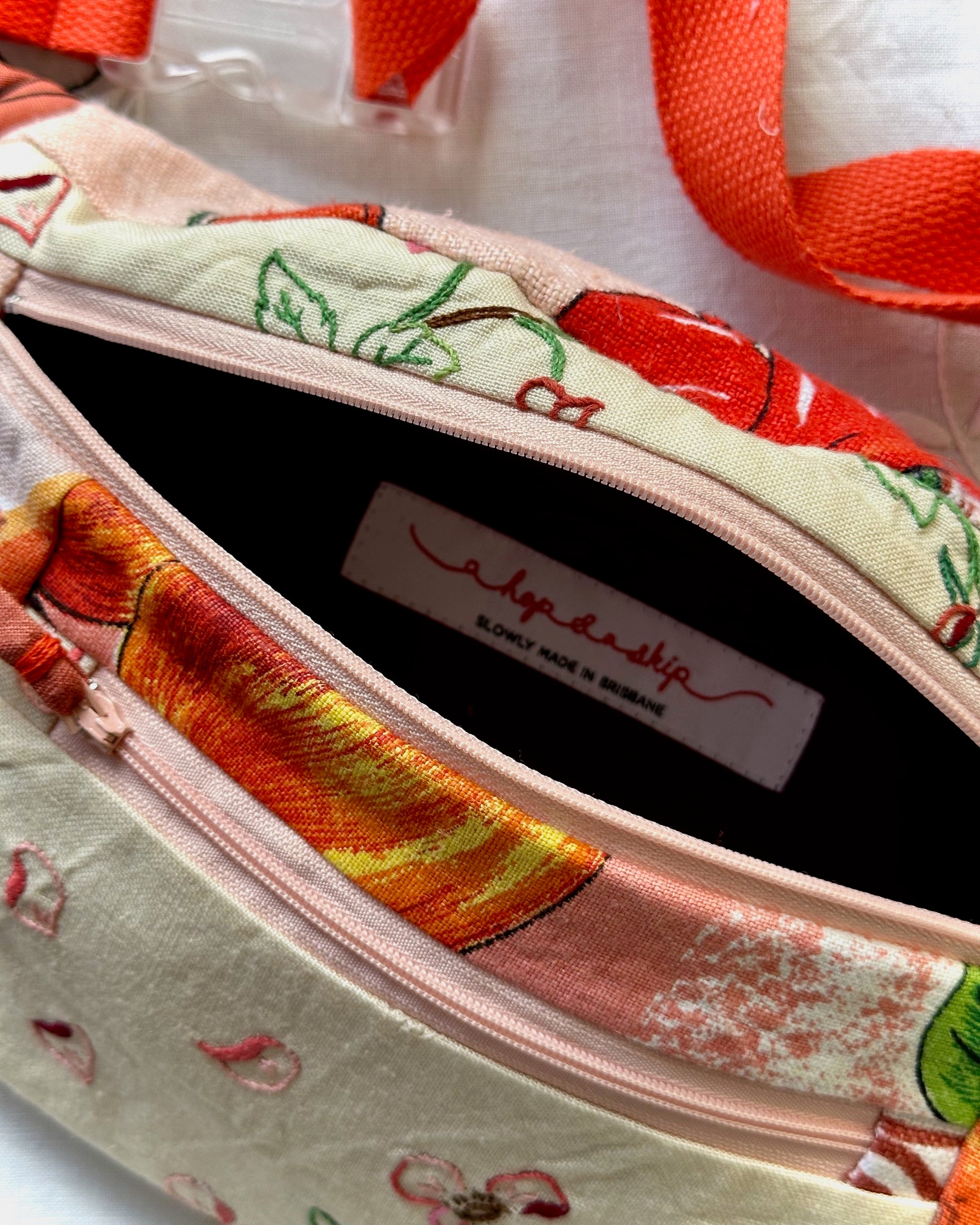 Close-up of a fabric zippered pouch with a colorful cherry and floral print, showing the interior lining and a visible 'a hop and a skip' brand label.