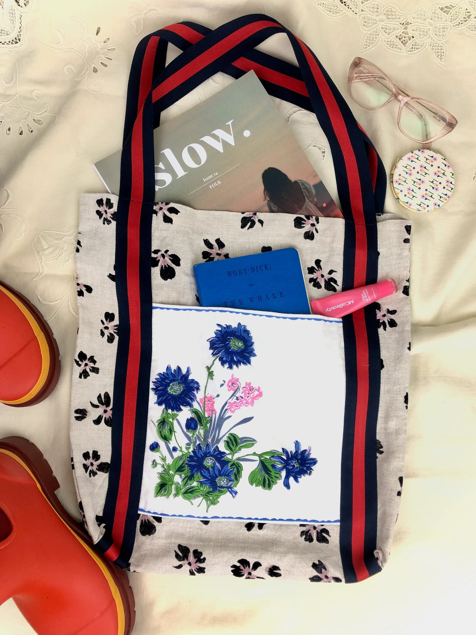 Flat lay of tote bag with Slow magazine, journal, reading glasses, lip gloss and Merry People gum boots