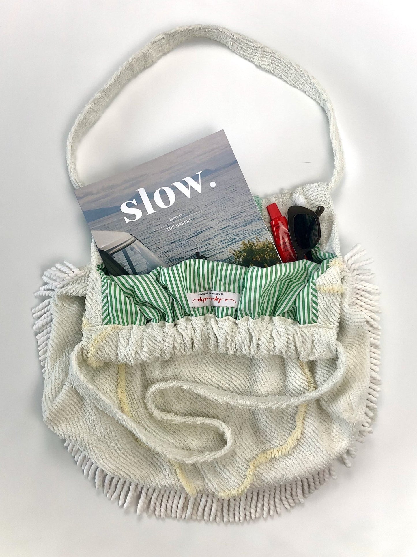 Flat lay of beach bag with Slow Journal magazine sunglasses and lippy